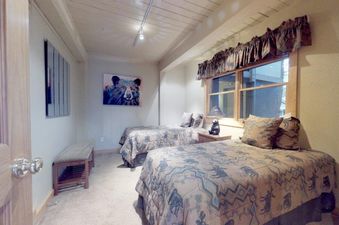 A cozy secondary bedroom at Top of the Village Summit 103 with two twin beds, a bear-themed artwork, and a window with wooden frames.