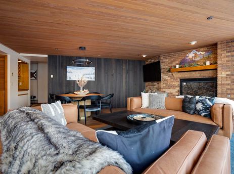 A spacious and inviting living area and dining space within the Chateau Chamonix CX114, featuring rustic elegant decor, leather sofas, a fireplace, and a dining table.