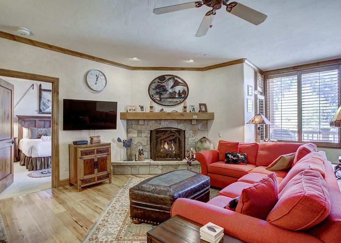 A spacious living room featuring a large red sectional sofa, a stone fireplace, and a wooden entertainment console with a TV mounted above it.