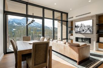 The interior of Moonlight Basin 204 Lakelodge features a large picture window offering a mountain view, a leather sofa with a contemporary fireplace, and a dining table with chairs.