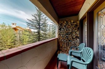 A balcony with two chairs and a stack of firewood beside a window with a view of the trees.