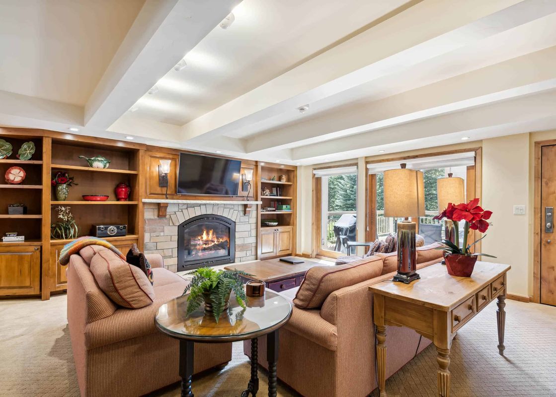 A cozy living room with a fireplace, couches, and a large window with a view of the outdoors.