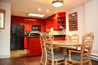 A kitchen with red cabinets and a dining table in front of a large window.