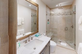 A modern bathroom with a white sink and vanity, white toilet and a large walk in shower with tiled walls.