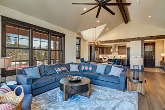 A living room with a large sectional sofa, a coffee table, and a view of the mountains outside the window.
