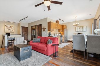 The image shows the open-concept living area and kitchen of Cana Loft 301, featuring a red sofa, a kitchen with wooden cabinets, and a dining area.