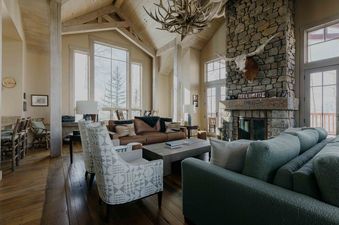 The living area of the Powder Place on Lower Galloping Goose features a soaring vaulted ceiling, a grand stone fireplace with a longhorn skull, and a comfortable arrangement of couches and armchairs.