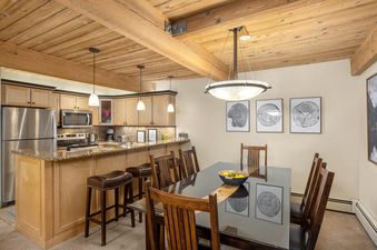 A dining table with chairs next to a fully equipped kitchen with wooden cabinetry in Trails 103.