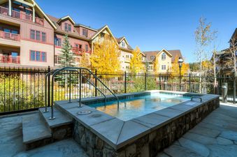A small hot tub with a stone patio and a fence in front of a complex of vacation rental homes.