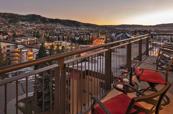 The private balcony offers stunning views of the snow-dusted town and surrounding mountains at dusk, with comfortable seating and a bottle of wine.