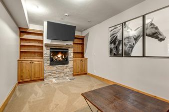 A cozy entertainment room at Deer Valley 355 B featuring a stone fireplace with a TV mounted above, flanked by built-in wooden shelving and cabinets.