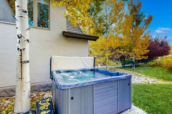 A private hot tub with bubbling water is situated next to a building with golden autumn trees in the background.