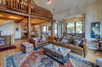 A cozy and rustic living area at Moonlight Mountain 1 Hidden Trail, featuring a large leather sectional, a patterned area rug, and an open-concept view of the kitchen and dining areas.