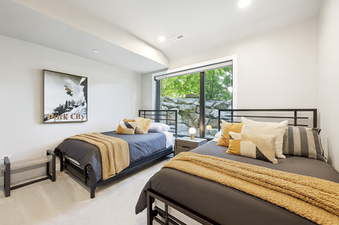 A modern bedroom with two beds, stylish yellow accents, and a large window overlooking a stone wall and trees at Holly Frost Chalet.