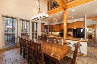 A large dining table with multiple chairs sits in the foreground, with a kitchen and a loft area in the background.
