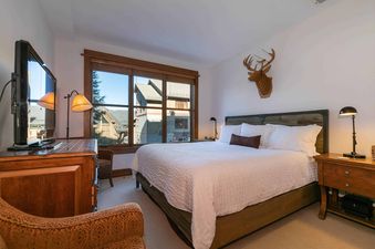 A bedroom with a large bed, a wooden dresser, and a window with a view of trees.