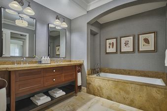 A modern bathroom features dual vanity sinks with dark wood cabinetry and a large marble-clad bathtub, illuminated by elegant sconces and recessed lighting.