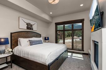 Blackstone 13th Green bedroom features a king-size bed, a flat-screen TV mounted above the fireplace, and a large window overlooking the mountains.