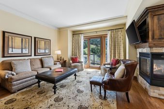 A lavish living room at the St Regis Madison Residence, featuring a cozy fireplace, comfortable seating, and a balcony with scenic mountain views.