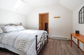 The bedroom at Southfork Retreat features a bed with a black metal frame and white and black patterned bedding, hardwood floors, a wooden desk, and a skylight.