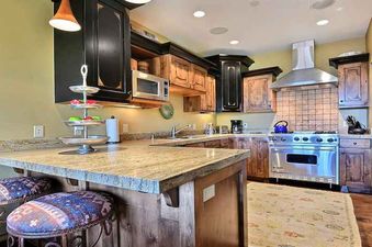 A modern rustic kitchen at Silver Star 102 with granite countertops, stainless steel appliances, and two patterned bar stools at the island.