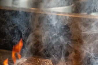 A seasoned steak searing over flames and smoke on a grill at Gravity Haus JH King.