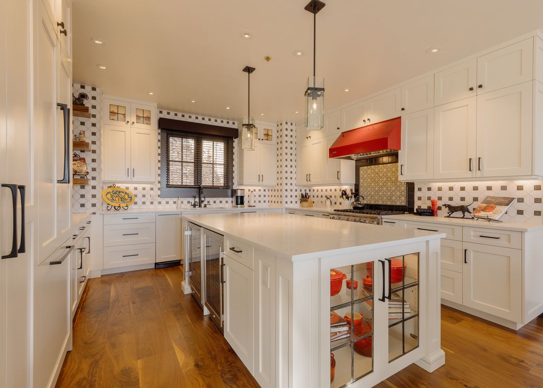 A spacious, modern kitchen with white cabinetry, a large central island, white countertops, and a striking red range hood in the Ivory Stone Chalet at See Forever.