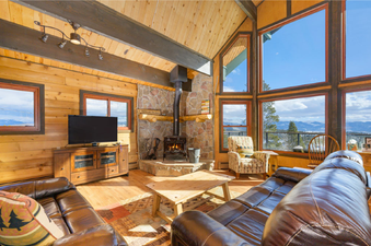 The living room at 273 Fallen Rock features a cozy fireplace, comfortable leather sofas, and large windows offering stunning mountain views.