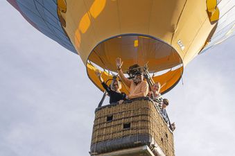 A group of people waves from a hot air balloon.
