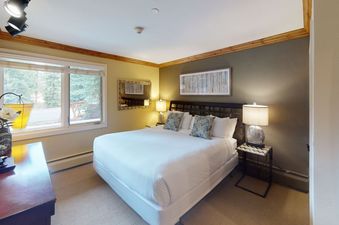 A bedroom with a king-sized bed, two nightstands, a large window, and a TV.
