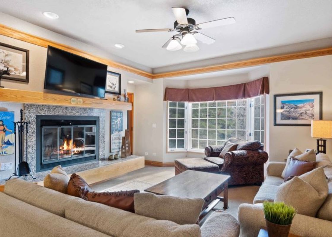 A spacious living room with comfortable sofas, a fireplace, and a large bay window overlooking the outdoors.
