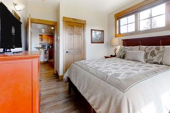 EagleRidge Lodge 203's bedroom features a comfortable king-sized bed with a beige and brown comforter, white pillows, and additional pillows with decorative patterns, as well as a bedside table with a lamp.