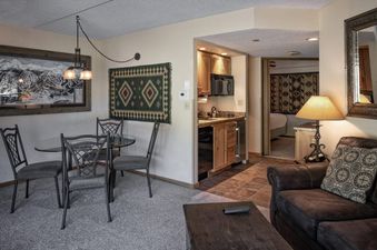 A view of the dining and living area inside the Colorado Suite Beaver Run Resort, featuring a glass dining table, leather sofa, and a compact kitchen.