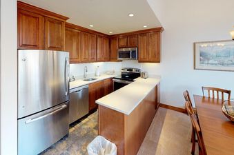 The kitchen at Manor Vail 348 has stainless steel appliances, wood cabinets, and a small dining area. The kitchen is well-equipped for preparing meals.