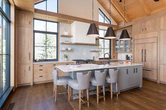 A modern kitchen with a large island and bar stools, white cabinets and a stainless steel stove.