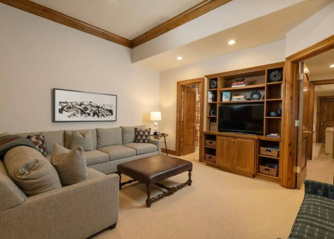 The living area features comfortable seating, a large entertainment center with a television, and elegant wood accents throughout the room.