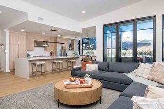 Modern living room with a sectional sofa, large windows with mountain views, and a wooden coffee table.