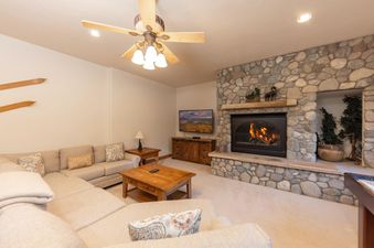 The living area of Fireside Lodge features a large sectional sofa, a coffee table, and a stone fireplace with a television mounted above it.