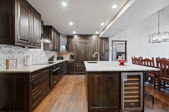 A modern kitchen at St James Place 437 features dark wood cabinetry, white countertops, a tiled backsplash, integrated appliances, a kitchen island with a wine cooler, and hardwood flooring.