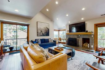 The living area features a brown leather sofa, a blue sofa, a fireplace, and a large flat-screen TV.