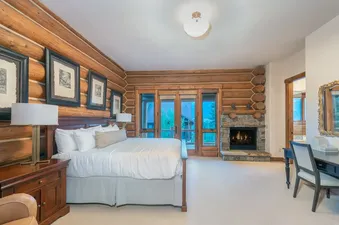 The bedroom at Tristant 125 features log walls, a large bed, a fireplace, and a desk, offering a rustic yet comfortable ambiance.