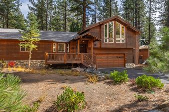 The North Shore Forest Haven is a beautiful cedar-sided house with a large wooden deck and garage, surrounded by tall pine trees and natural landscaping.