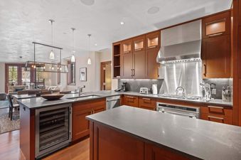 A modern kitchen in Solaris 4EE features rich wood cabinetry, stainless steel appliances, a large island with a wine cooler, and dark countertops, seamlessly blending into a comfortable living area.