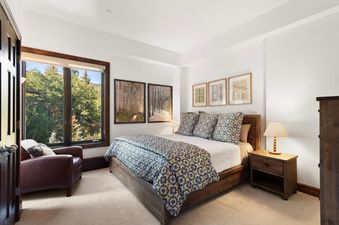 Comfortable bedroom at Chamonix 50 featuring a queen-sized bed, armchair, and a view of the forest.