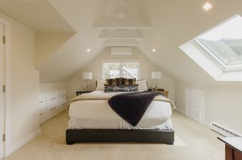A serene bedroom in Smugglers Hideaway, featuring a bed with plush bedding, bedside tables, built-in storage, and a window with a skylight.