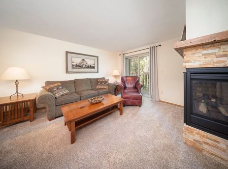 A cozy living room at Beaver Village 1123, featuring a comfortable sofa, an armchair, a fireplace, and a large window.
