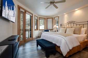 A cozy bedroom with a large bed, a TV showing a snowy mountain, and windows overlooking a winter landscape.