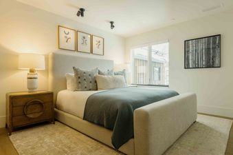 A cozy bedroom is elegantly furnished, featuring a large bed with a light grey upholstered headboard and base, soft white and grey bedding, and a muted teal throw blanket.