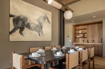 A modern dining room at the Little Thunder Chalet features a long dark wood table set with white dishes and clear glasses.