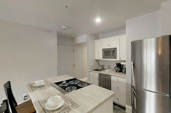 A modern kitchen with stainless steel appliances, white cabinets, and a central island with a stovetop and two place settings.